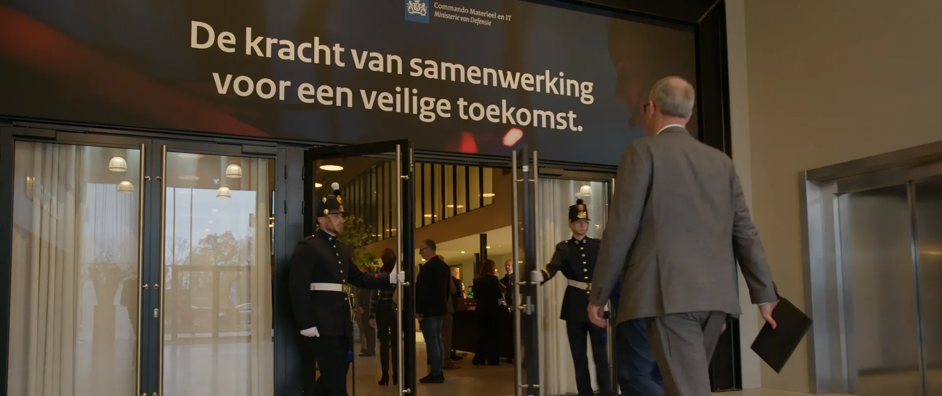 De entree van het IT-leveranciers evenement 2025, waarbij mannen in een ouderwets politiepak de deur openen voor een gast.