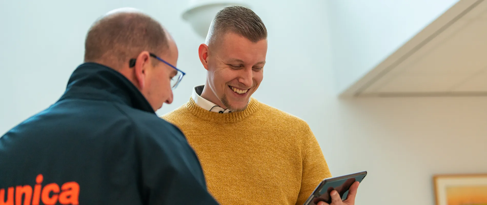 Twee medewerkers van Unica in gesprek; één in Unica-jas en één in okergele trui bekijkt lachend een tablet.  Deze tekst is kort, beschrijvend en geschikt voor gebruik op een website (inclusief de nieuwe corporate site). Laat me weten als je een alternatieve insteek wilt, zoals formeler of met focus op technologie.