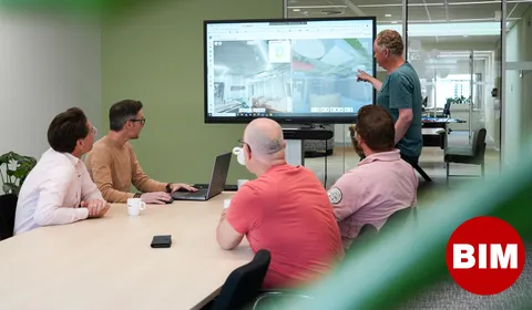 Bim coordinators in overleg en iets aanwijzend op grote scherm met bim stip
