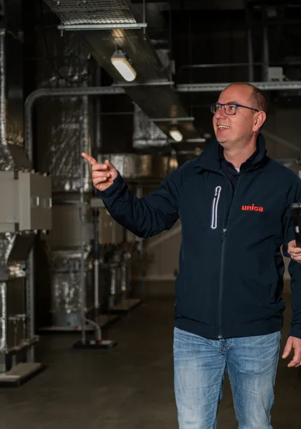 "Twee medewerkers van Unica Watertechniek inspecteren een technische ruimte met HVAC-installaties, gericht op efficiënte en veilige wateroplossingen."