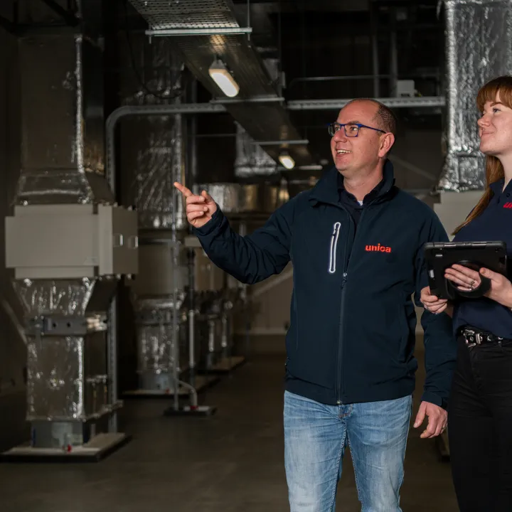 "Twee medewerkers van Unica Watertechniek inspecteren een technische ruimte met HVAC-installaties, gericht op efficiënte en veilige wateroplossingen."