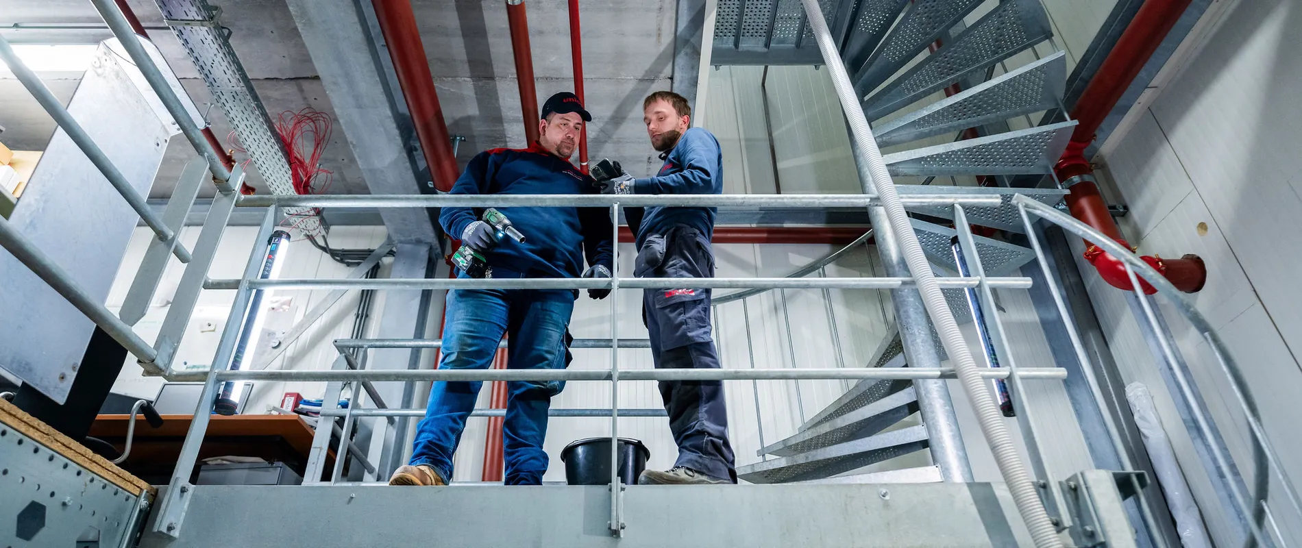 Twee Unica-monteurs overleggen tijdens werkzaamheden aan sprinklerleidingen op een technische verdieping.