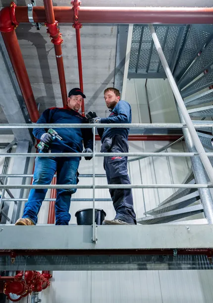 Twee Unica-monteurs overleggen tijdens werkzaamheden aan sprinklerleidingen op een technische verdieping.