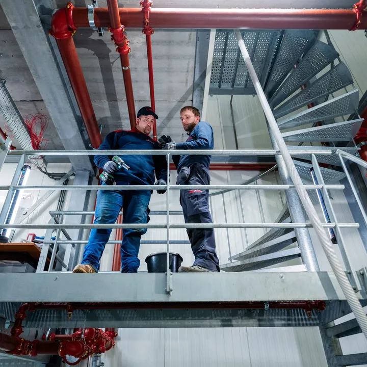 Twee Unica-monteurs overleggen tijdens werkzaamheden aan sprinklerleidingen op een technische verdieping.