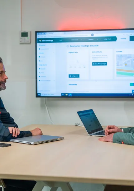 Twee mannen in overleg bij Unica over energiemanagementsystemen met een dashboard op het scherm.