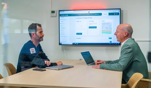 Twee mannen in overleg bij Unica over energiemanagementsystemen met een dashboard op het scherm.