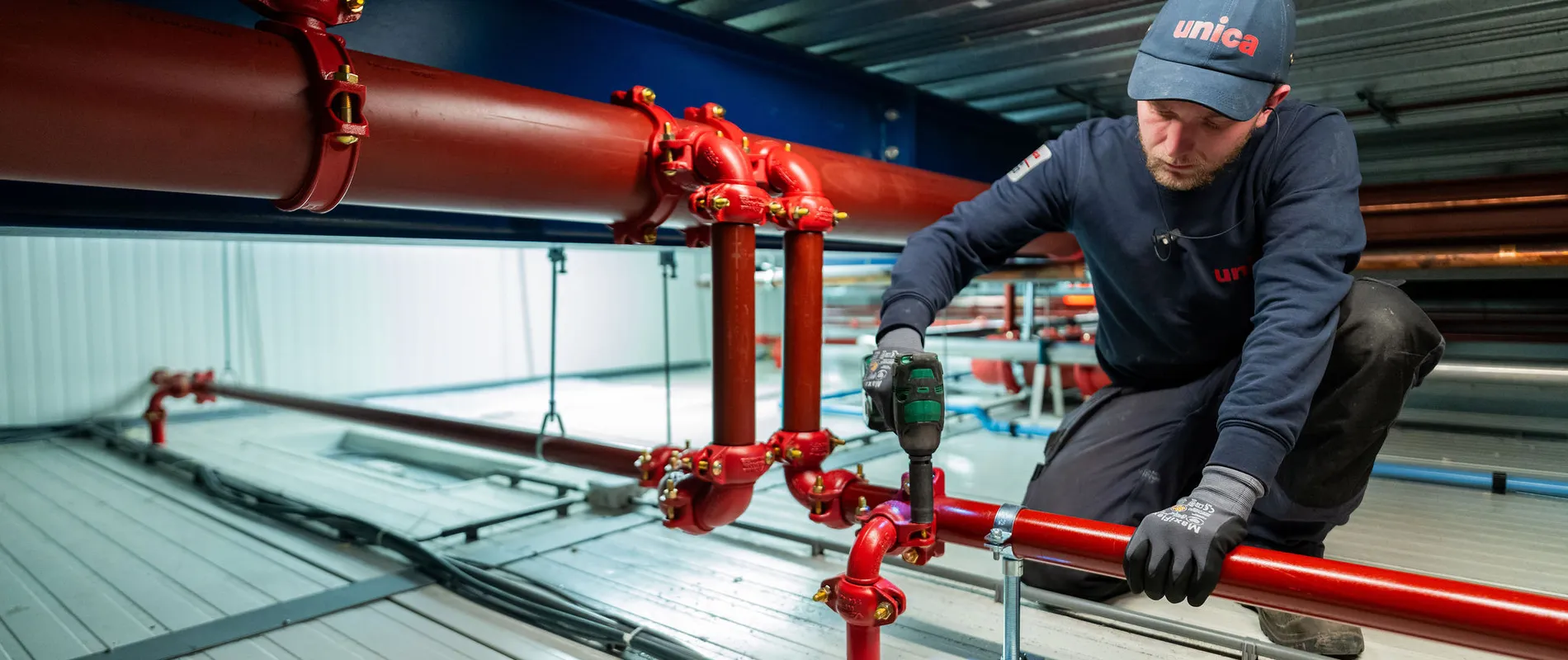 Unica-monteur voert montage- en onderhoudswerkzaamheden uit aan sprinklerleidingen op hoogte.