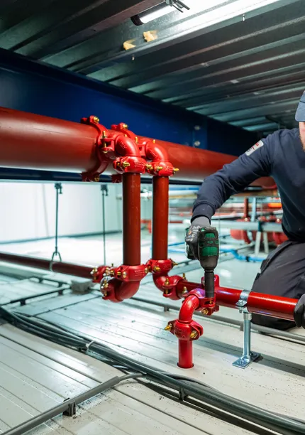 Unica-monteur voert montage- en onderhoudswerkzaamheden uit aan sprinklerleidingen op hoogte.