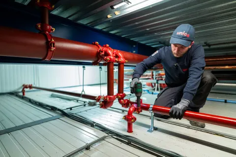 Unica-monteur controleert technische tekeningen tijdens werkzaamheden aan een sprinklerinstallatie.