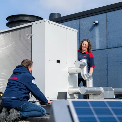 Unica-technici werken op het dak aan een installatie, met leidingen en zonnepanelen op de voorgrond.