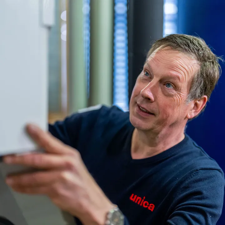 Unica-monteur voert handmatige controle uit op installatiepaneel tijdens onderhoudsronde.
