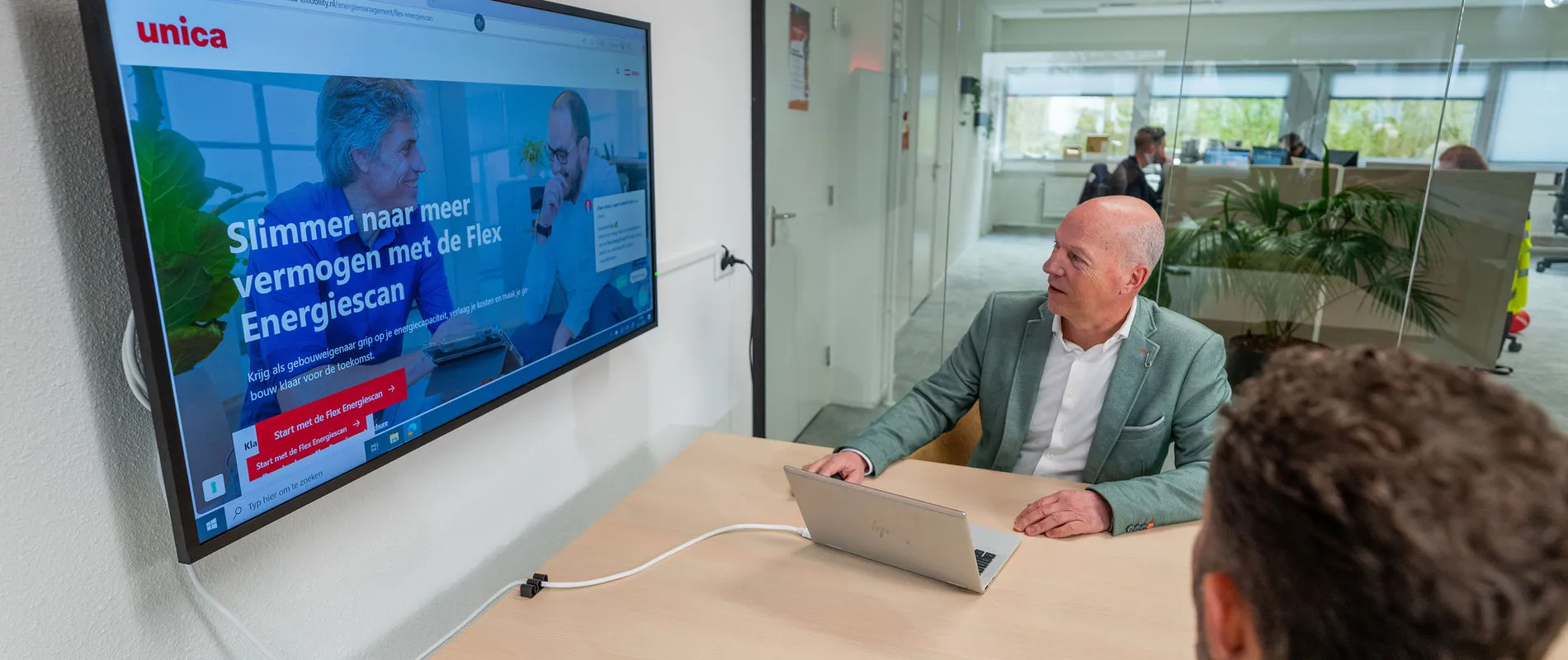 Collega’s in overleg terwijl de Flex Energiescan zichtbaar is op het scherm in een vergaderruimte.
