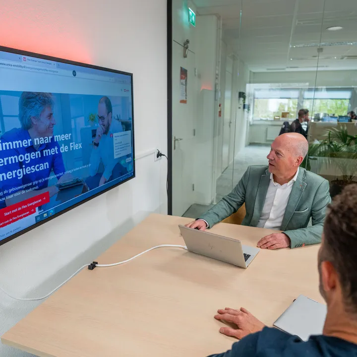 Collega’s in overleg terwijl de Flex Energiescan zichtbaar is op het scherm in een vergaderruimte.
