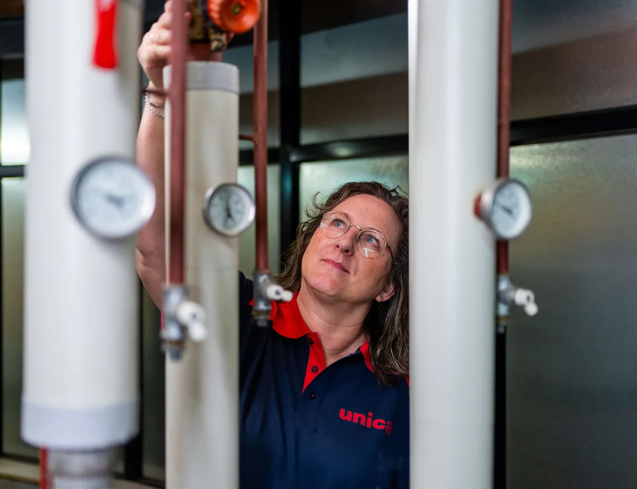 Unica-technicus inspecteert leidingen en meters in installatieruimte met focus op regelgeving.