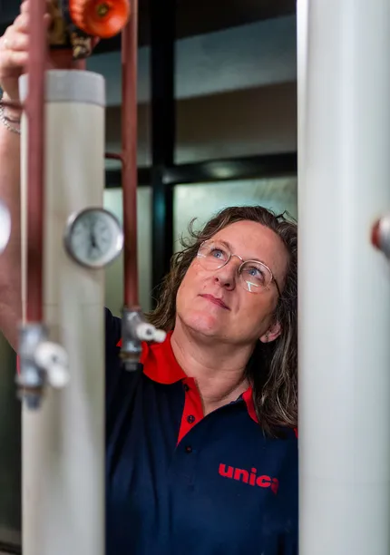 Unica-technicus inspecteert leidingen en meters in installatieruimte met focus op regelgeving.