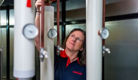 Unica-technicus inspecteert leidingen en meters in installatieruimte met focus op regelgeving.