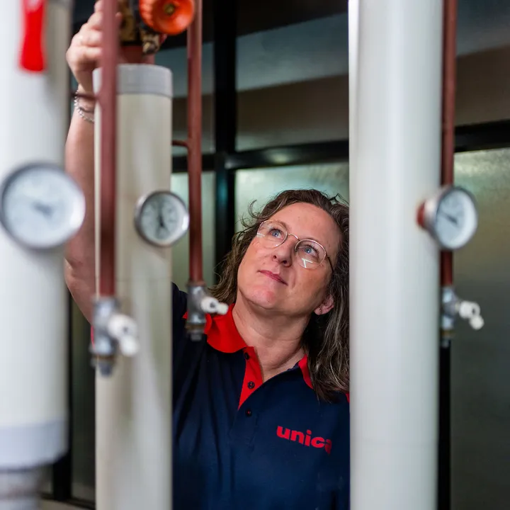 Unica-technicus inspecteert leidingen en meters in installatieruimte met focus op regelgeving.