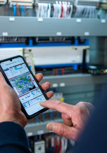 Unica technicus gebruikt smartphone om elektrotechnische installatie te monitoren in schakelkast bij gebouwbeheer.