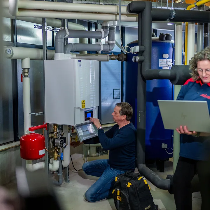 Monteurs voeren controle en onderhoud uit aan verwarmingsinstallatie met digitale ondersteuning.