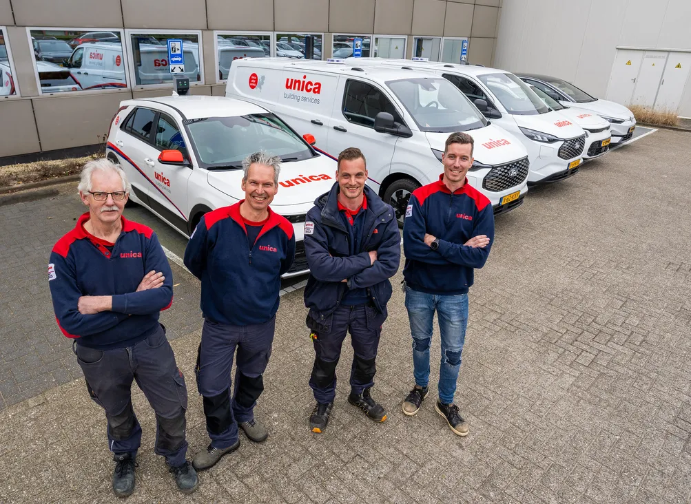 Vier monteurs van Unica Installatietechniek poseren voor een rij bedrijfswagens op het terrein van een Unica-locatie.