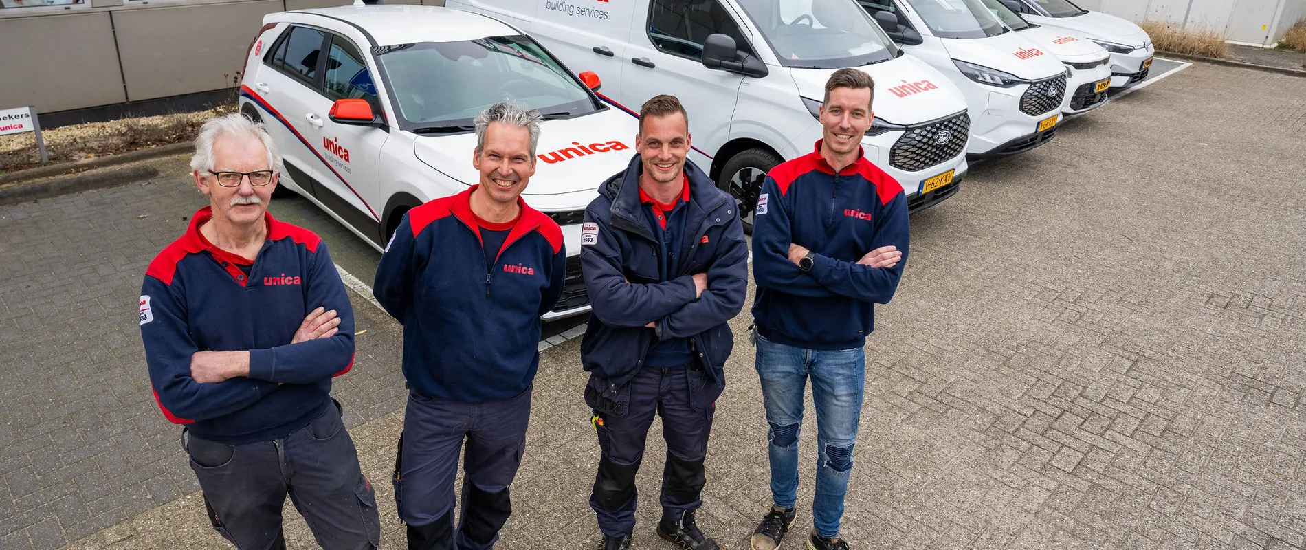 Vier monteurs van Unica Installatietechniek poseren voor een rij bedrijfswagens op het terrein van een Unica-locatie.