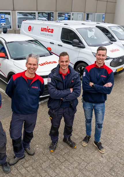 Vier monteurs van Unica Installatietechniek poseren voor een rij bedrijfswagens op het terrein van een Unica-locatie.