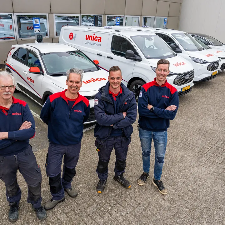 Vier monteurs van Unica Installatietechniek poseren voor een rij bedrijfswagens op het terrein van een Unica-locatie.