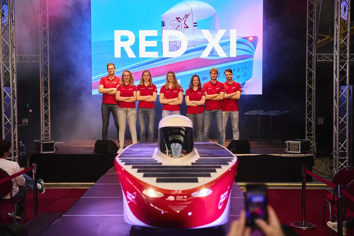 De zeven teamleden van Solar Team Twente staan op een podium, op de voorgrond staat de zonnewagen