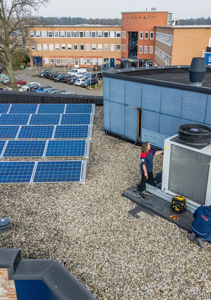Een foto van boven van het dak van een gebouw staan rijen zonnepanelen en een HVAC installatie waar twee medewerkers van Unica aan het werk zijn