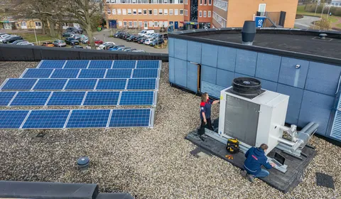 Een foto van boven van het dak van een gebouw staan rijen zonnepanelen en een HVAC installatie waar twee medewerkers van Unica aan het werk zijn