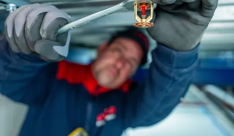 Unica-monteur voert onderhoudswerk uit aan een sprinklermondstuk in een technische ruimte.