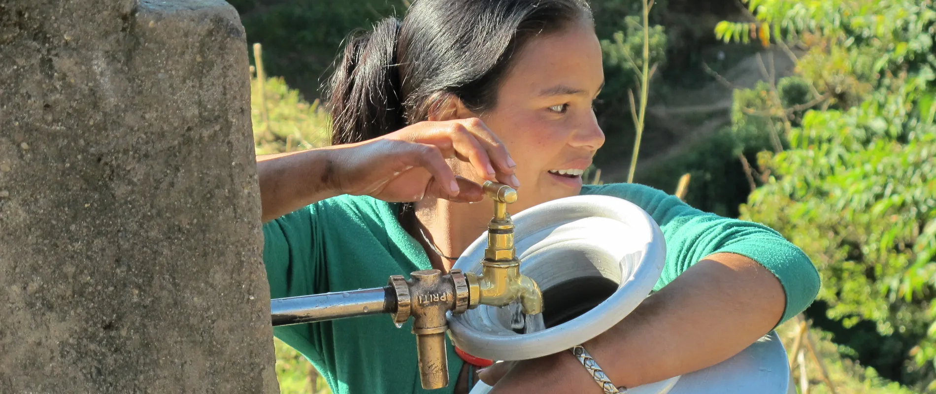 Lachende vrouw met waterkan bij een kraan waar water uit stroomt