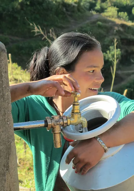 Lachende vrouw met waterkan bij een kraan waar water uit stroomt