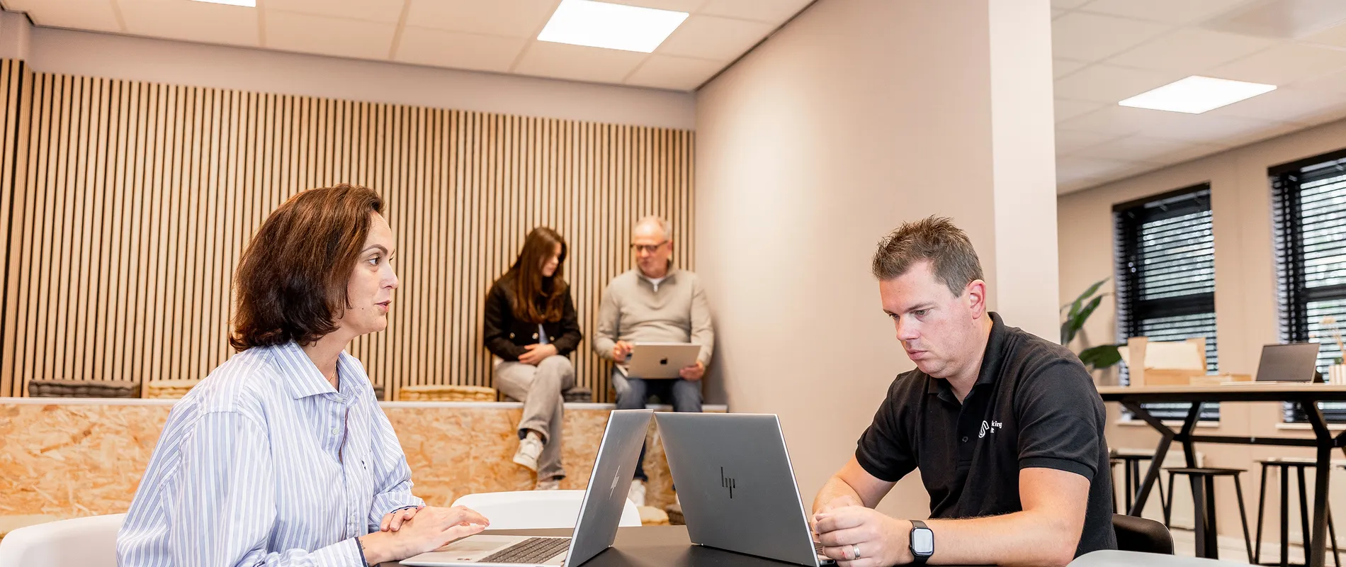 Twee Working Spirit medewerkers werken op een laptop met twee collega's op de achtergrond