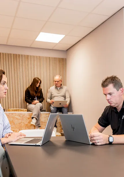 Twee Working Spirit medewerkers werken op een laptop met twee collega's op de achtergrond
