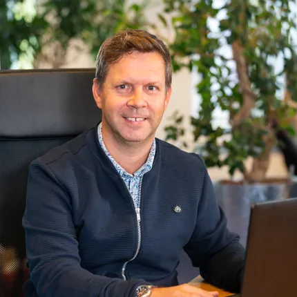 Projectmanager Leon Blom van Unica Building Projects lacht terwijl hij achter de laptop aan het werk is
