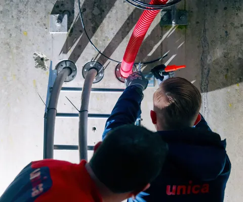 Two people working with cables in an industrial setting. One is holding a red conduit, illuminating the work area with a flashlight.