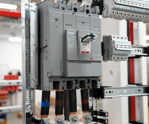 A close-up of a large electrical circuit breaker installed on a metal frame with attached cables in an industrial setting.