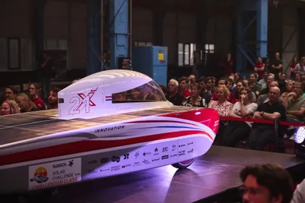 Een zaal vol mensen kijkt naar het podium waar de zonnewagen van Solar Team Twente staat
