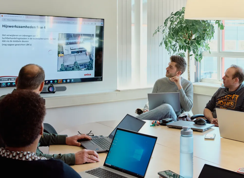 Medewerkers van Unica zitten in overleg en bekijken een presentatie op een beeldscher,