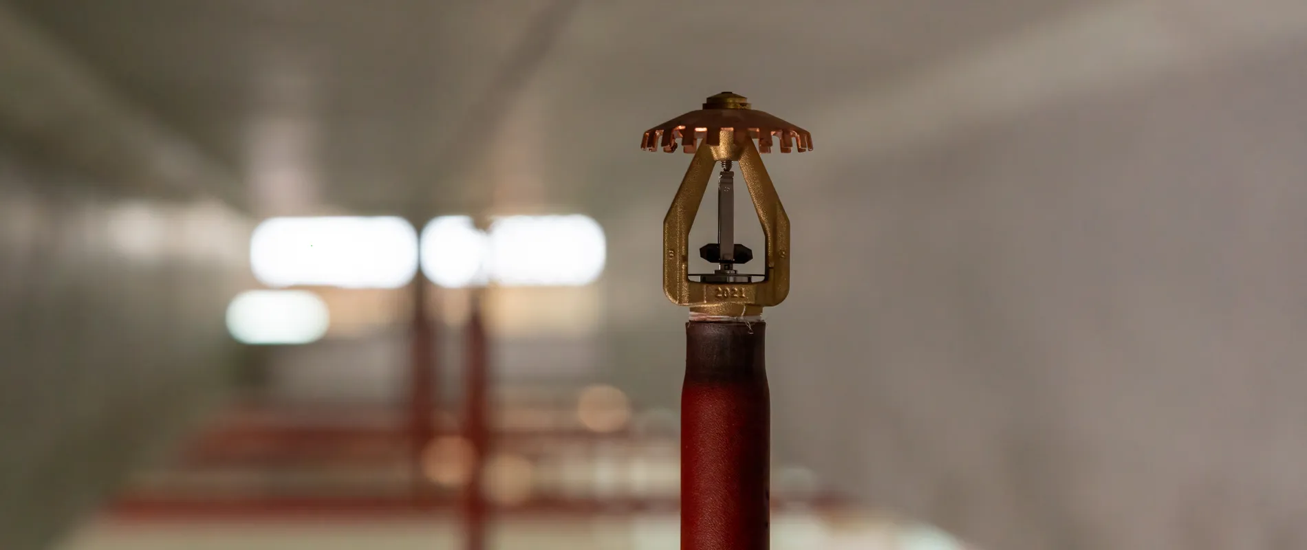 Close-up van een sprinklerkop op een rood leidingwerk in een logistieke omgeving.