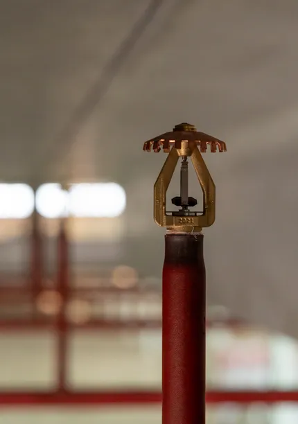 Close-up van een sprinklerkop op een rood leidingwerk in een logistieke omgeving.