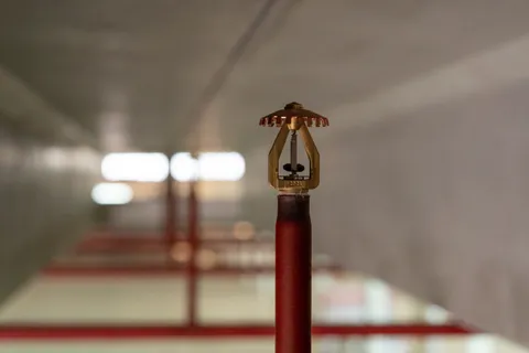 Close-up van een sprinklerkop op een rood leidingwerk in een logistieke omgeving.