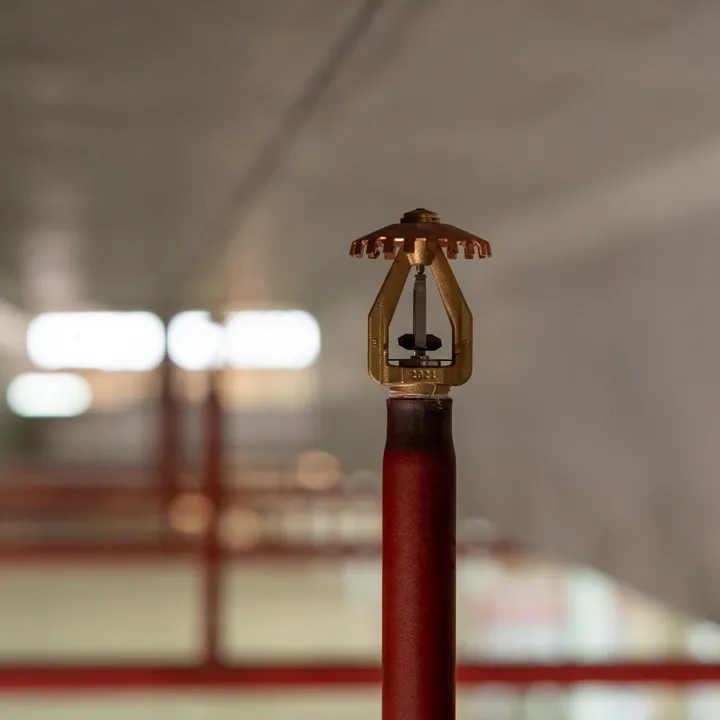 Close-up van een sprinklerkop op een rood leidingwerk in een logistieke omgeving.