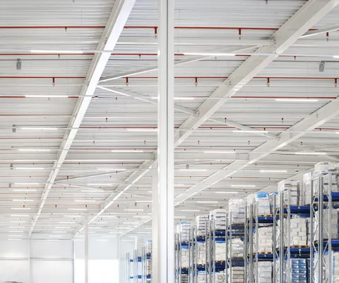 Plafond van een magazijn met zichtbaar leidingwerk van een sprinklerinstallatie boven opslagrekken
