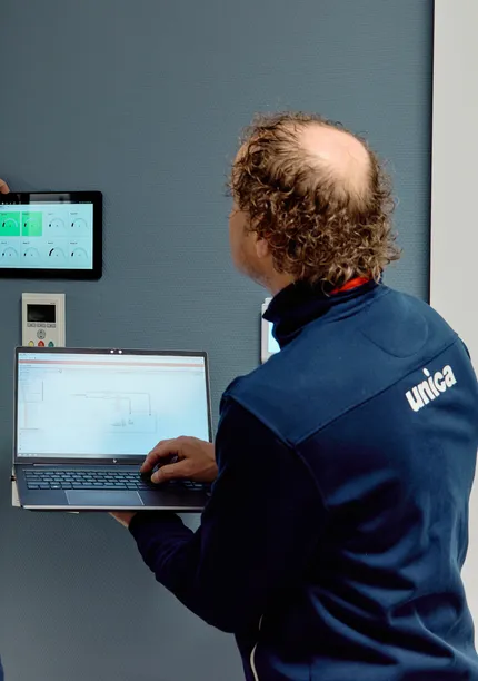 Twee medewerkers van Unica checken de status van de regeltechnische installatie via wandpaneel en laptop