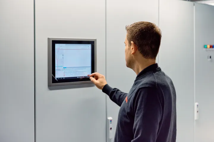 Medewerker van Unica checkt het gebouwautomatiseringssysteem via een wandpaneel