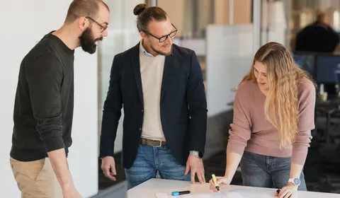 Twee mannen en een vrouw houden werkoverleg aan een tafel