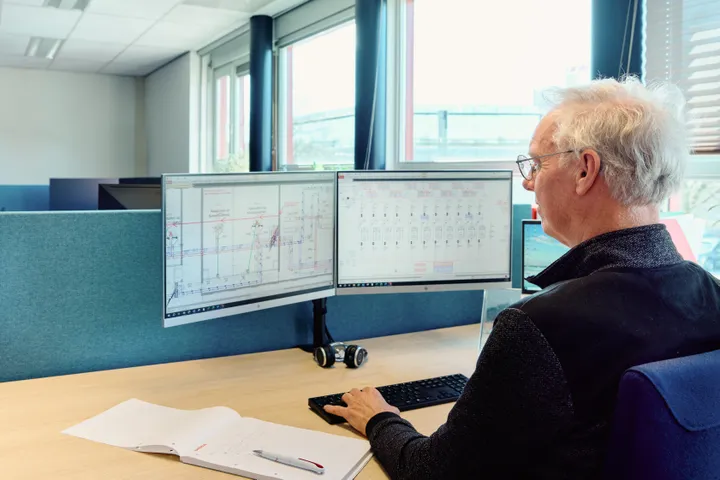Medewerker van Unica zit achter bureau en bekijkt schematische tekeningen van installaties