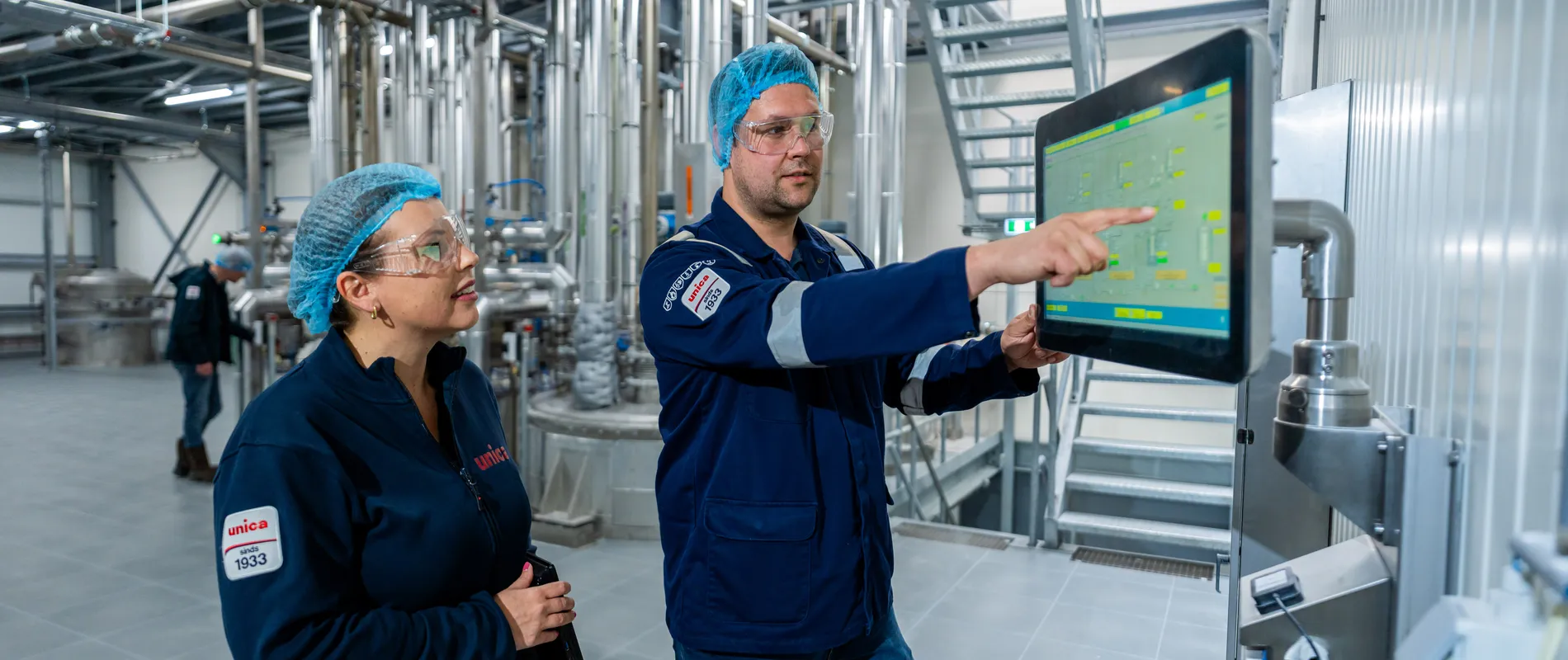 Unica-engineers bespreken een digitaal besturingssysteem via een groot HMI-touchscreen voor procesbewaking.